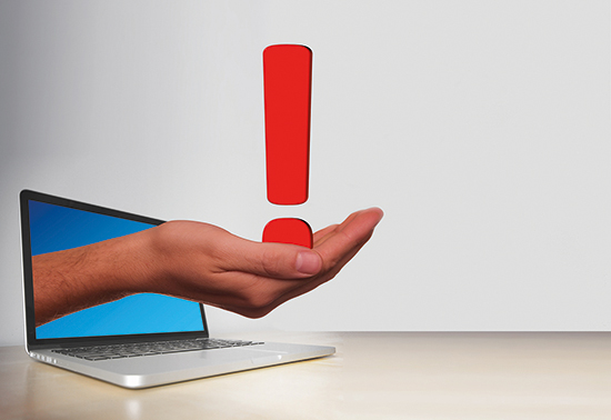 Aus dem Bildschirm eines aufgeklappten Laptops ragt eine Hand, die ein großes, rotes Ausrufezeichen hält