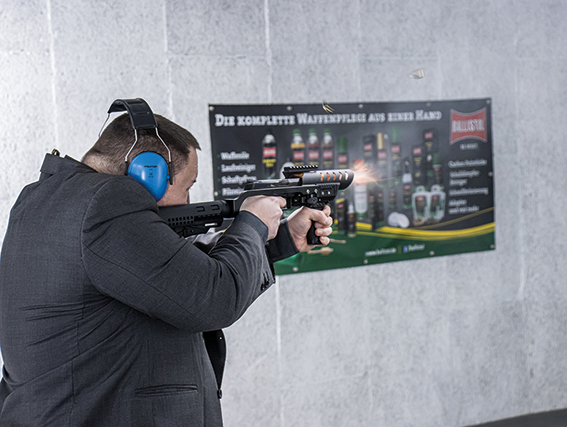 Ein Schütze am Schießstand mit Gehörschutz, der gerade eine Pistole abfeuert