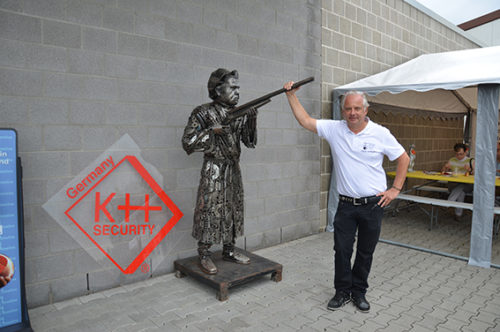 Eine Oma mit einem Gewehr in der Hand als Metall-Statue. Sie ist das Wahrzeichen der Firma. Rechts steht Klaus Hofmann