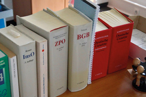 Eine Reihe von Büchern mit dem Thema Steuerrecht, die auf einem Schreibtisch stehen. Im Vordergrund sieht man ein Stempelkarussel