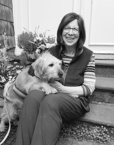Eine Frau mit einem Hund sitzt auf einer Treppe und lächelt in die Kamera. Das Bild ist in Schwarz/Weiß