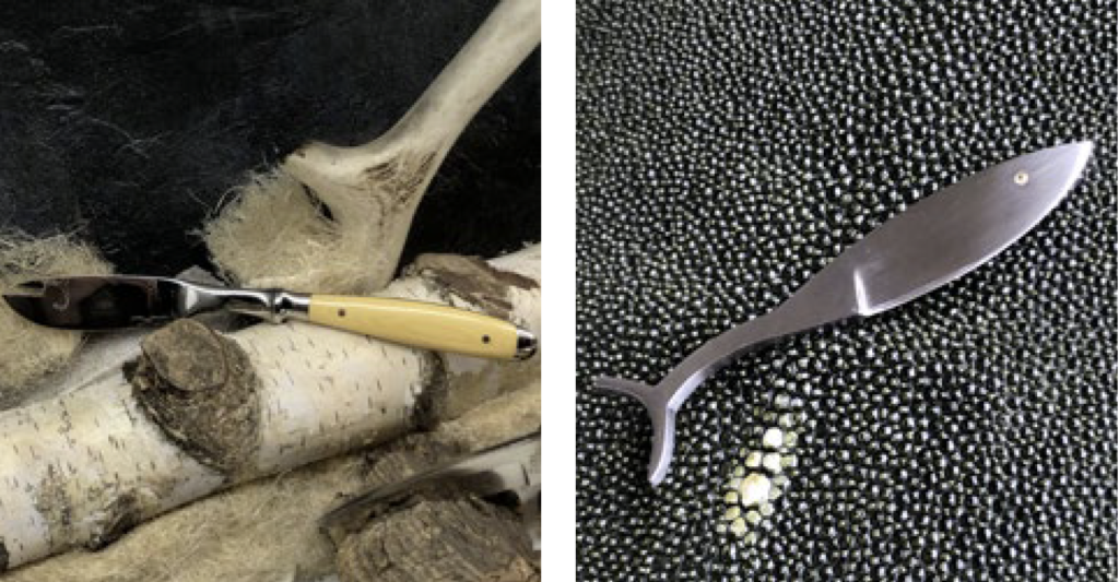 links ein Sardinenmesser von PUMA dekoriert auf einem Birkenstamm; rechts ein fischförmiges Messkelchen mit einem Brillanten als Auge